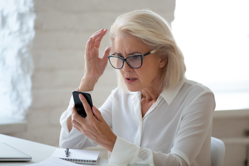 Elderly woman confused and stressed looking at a cell phone.